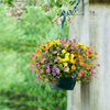 A vibrant mixed bouquet of silk daisies in yellow, purple, and orange flowers hanging on a stone wall.