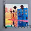 A magnet featuring a vibrant sunset scene with palm trees and a modern blue building overlooking the ocean.
