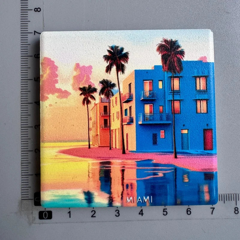 A magnet featuring a vibrant sunset scene with palm trees and a modern blue building overlooking the ocean.