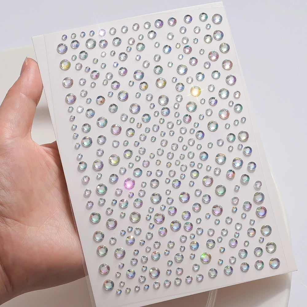 A hand holds a sheet of glitter gem stick-on facial tattoos showing various colored gems.