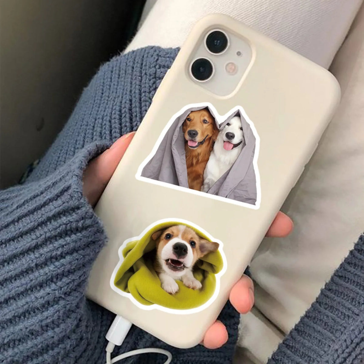 A hand holds a phone displaying stickers of dogs in hoods against a light background.