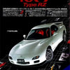 A white Mazda RX-7 sports car model displayed on a black surface with various parts and accessories below.
