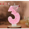 Pink glitter number three birthday candle with a crown topper on a wooden base