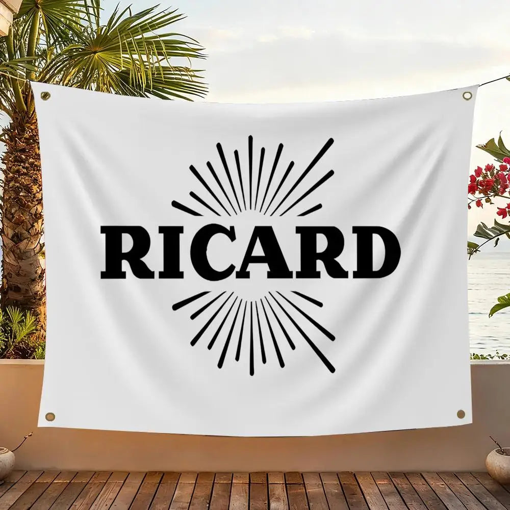 A white flag featuring the name RICARD in black text with a sunburst design, displayed outdoors.