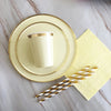A gold disposable party tableware set featuring plates, a cup, and straws arranged on a light surface.