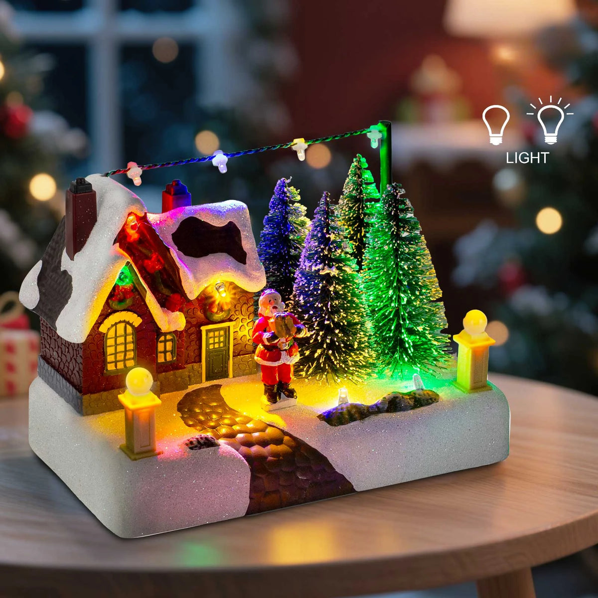 Illuminated Christmas village scene featuring a house, Santa, and snowy evergreen trees with string lights.
