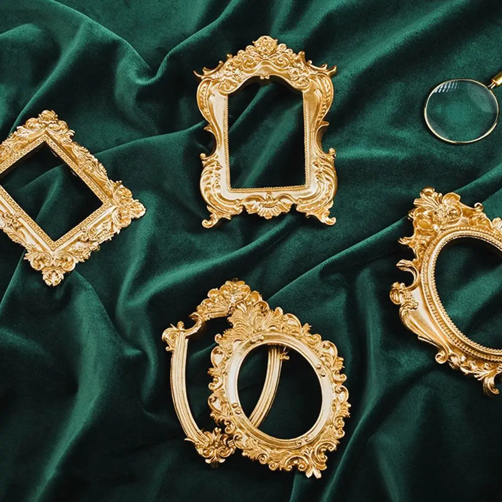 Several ornate vintage gold frames and decorative borders displayed on a dark emerald green velvet fabric.