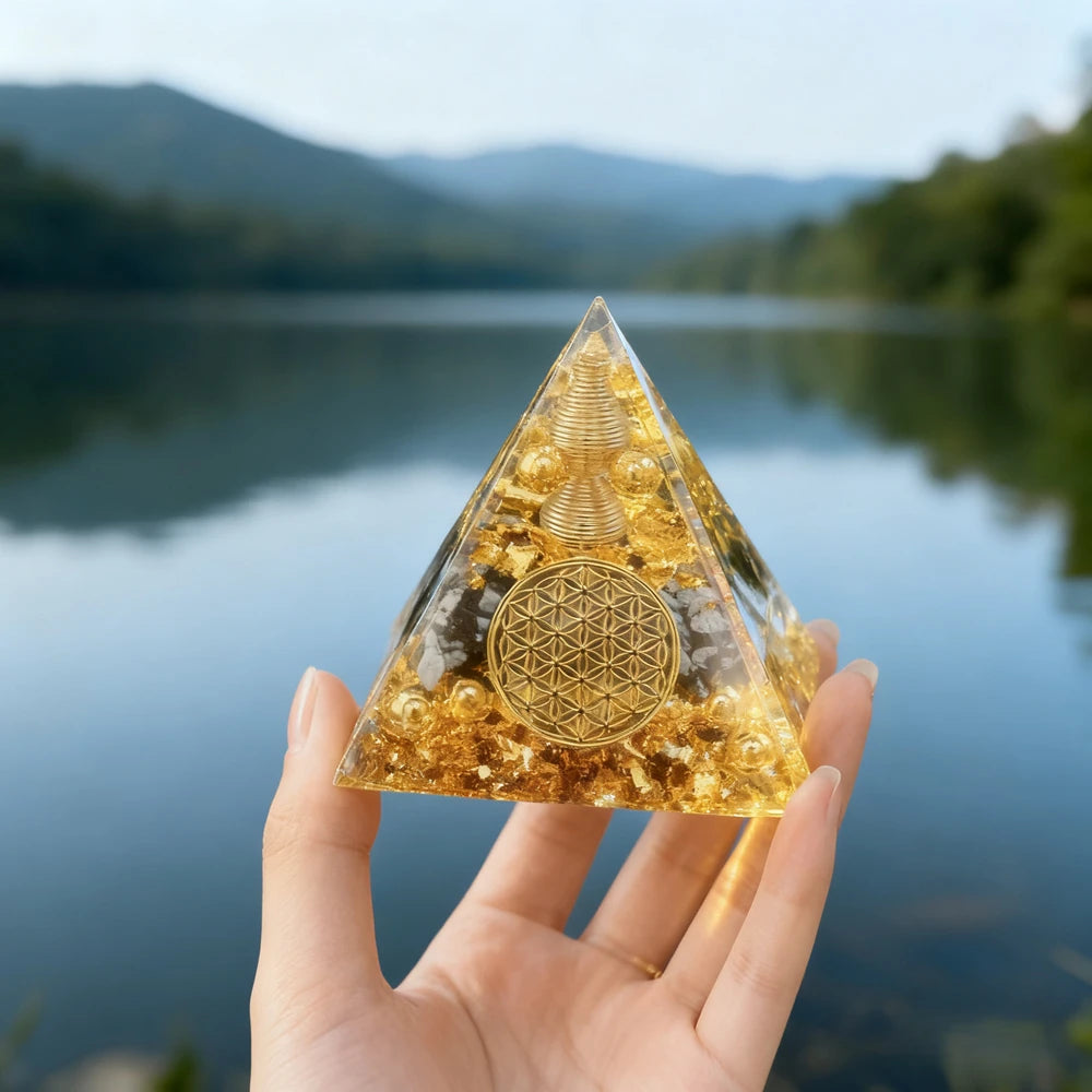 Hand holding a clear resin pyramid made with natural golden obsidian and copper coils against a lake background
