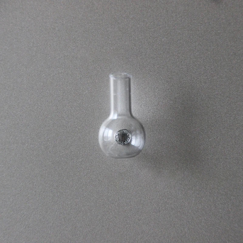 A clear glass fridge magnet with a narrow neck and a circular depression on the base.