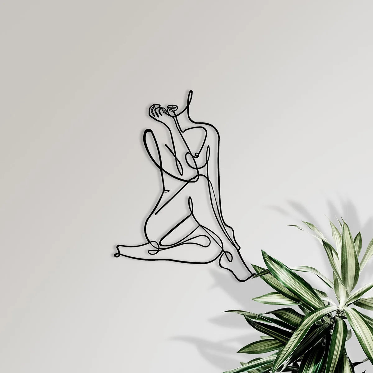 Black line art drawing of a nude female figure in a reclining pose on a light gray wall.