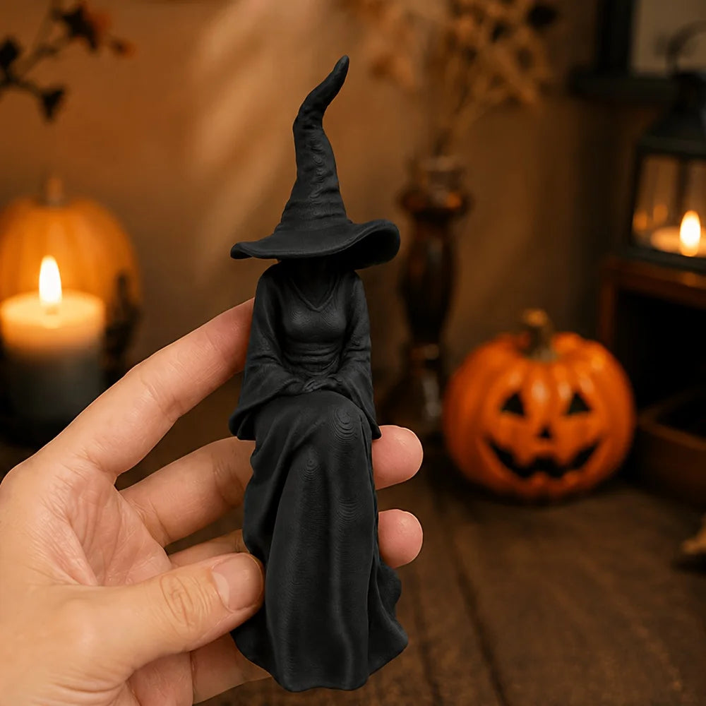 A black figurine of a witch in a pointed hat and flowing robe is held by a hand against a background with pumpkins.
