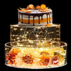 A tiered cake display featuring an orange and white cake under a clear acrylic stand illuminated by warm LED lights.