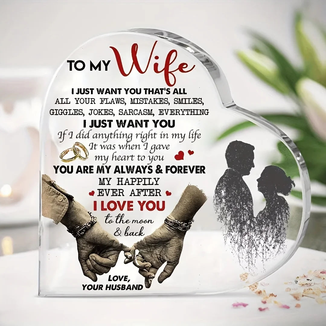 A clear heart-shaped acrylic decoration featuring a silhouette of a couple's hands and heads with romantic text.