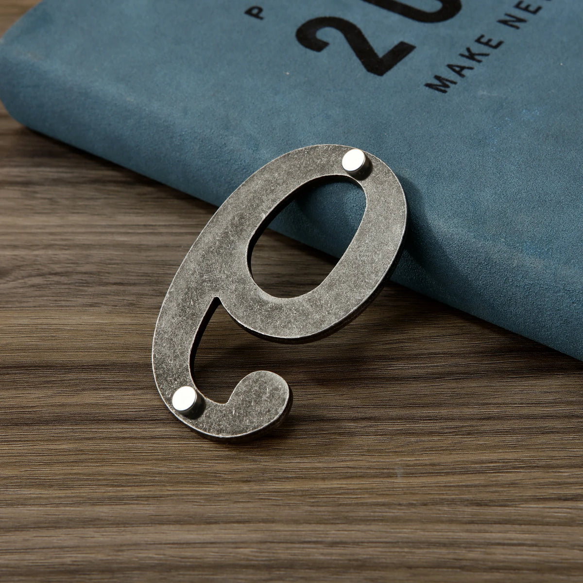 A silver magnetic house number cutout shaped like the letter E resting on a dark blue book.