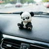 A cute angry panda figurine sitting on a car dashboard.