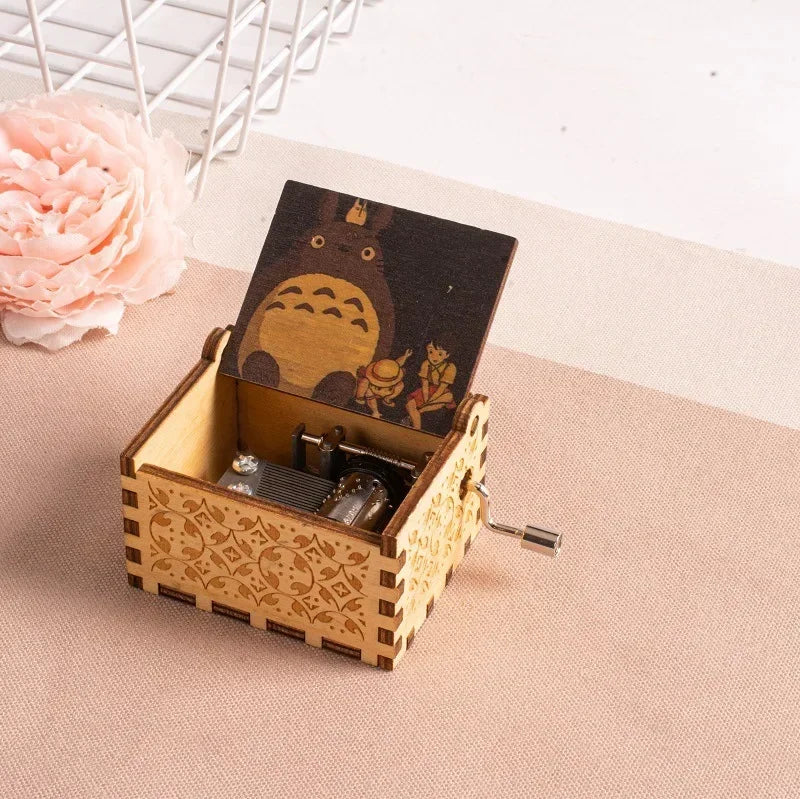 A hand-cranked wooden music box featuring a Totoro design, set against a light beige background.