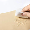 Una mano está aplicando un parche de cuero PU autoadhesivo sobre una superficie beige.