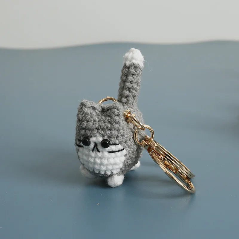 A handcrafted gray crochet cat keychain pendant resting on a smooth blue-gray surface.