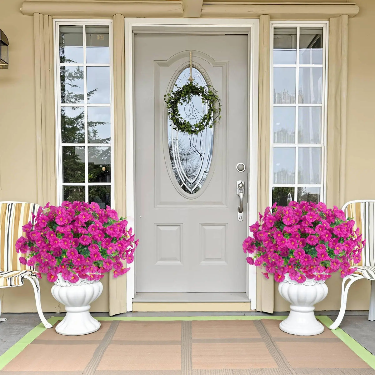 A front door decorated with a wreath and flanked by large potted pink flowers on a wooden floor.