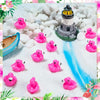 Pink resin flamingo duck figurines scattered on white snow with a decorative lighthouse in the background