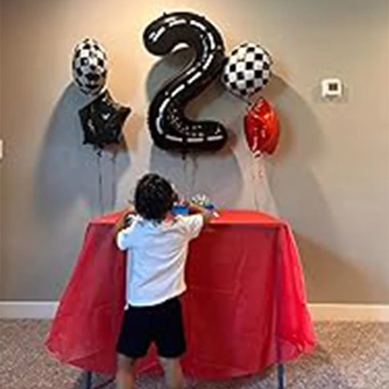 A person stands in front of a red draped table decorated with large black number balloons and a red car balloon for a birthda