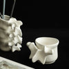 A white ceramic vase shaped like vertebrae is shown on a dark surface with a piece of paper nearby.