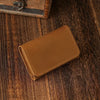 A brown leather card holder is placed on a dark wooden surface next to an old box.
