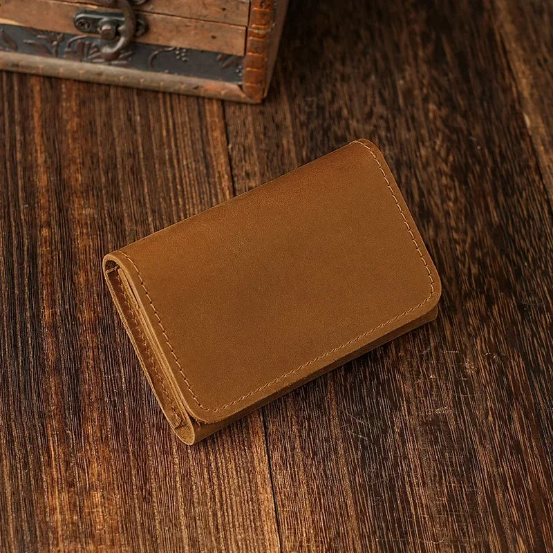 A brown leather card holder is placed on a dark wooden surface next to an old box.