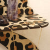 A gold chain necklace is displayed on a leopard print storage rack next to a purple crystal.