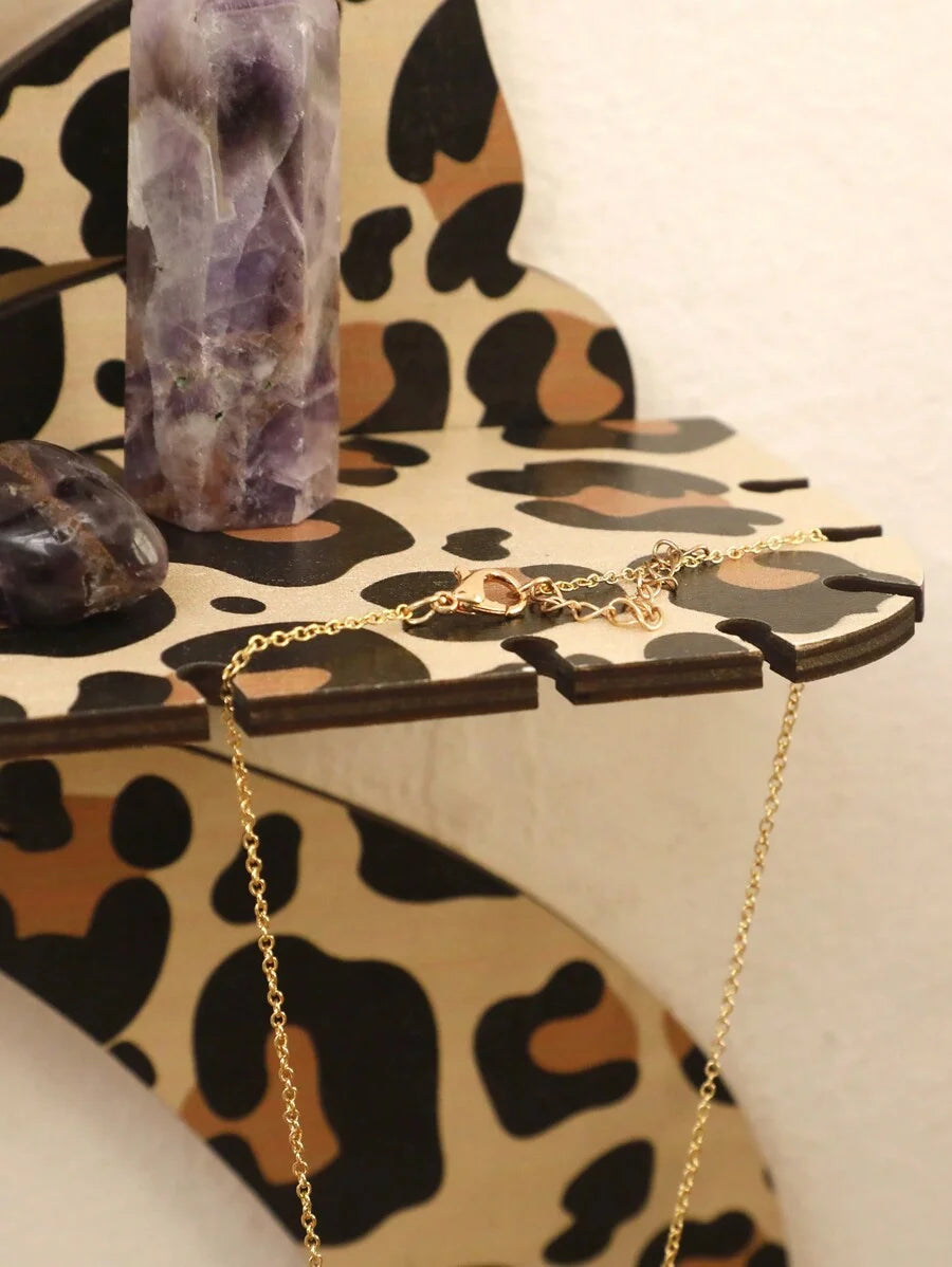 A gold chain necklace is displayed on a leopard print storage rack next to a purple crystal.