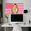 A woman with blonde hair is featured on a pink and white American flag tapestry hanging above a desk.