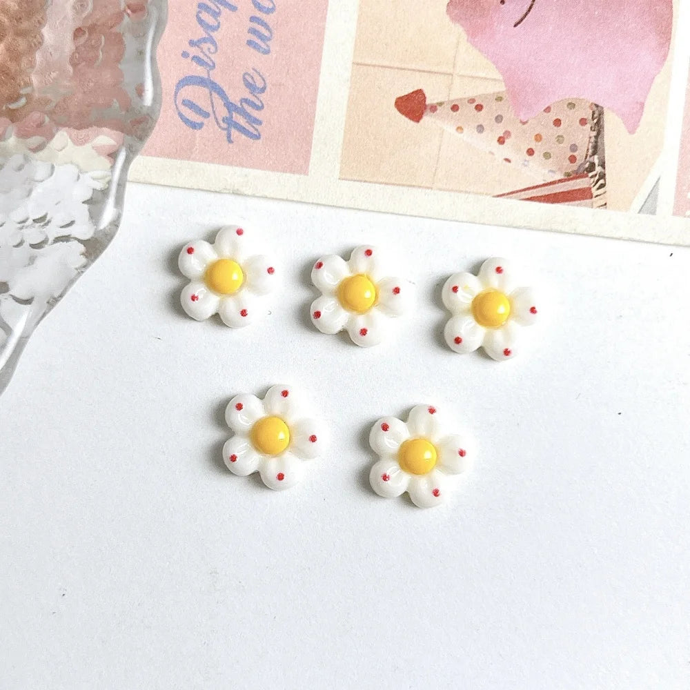 A set of six white and yellow flower resin nail art charms displayed on a white background next to a piece of paper.