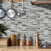 A gray marble tile wall sticker is displayed on a wooden countertop, with kitchen utensils hanging above it.