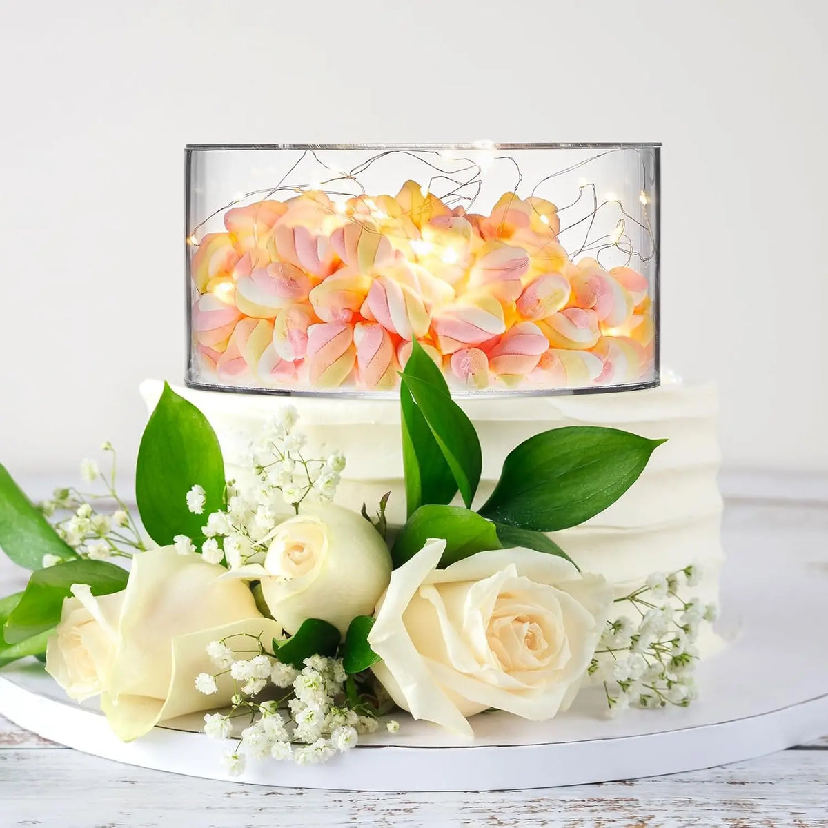 Clear acrylic cake display stands featuring glowing floral arrangements on a white cake.