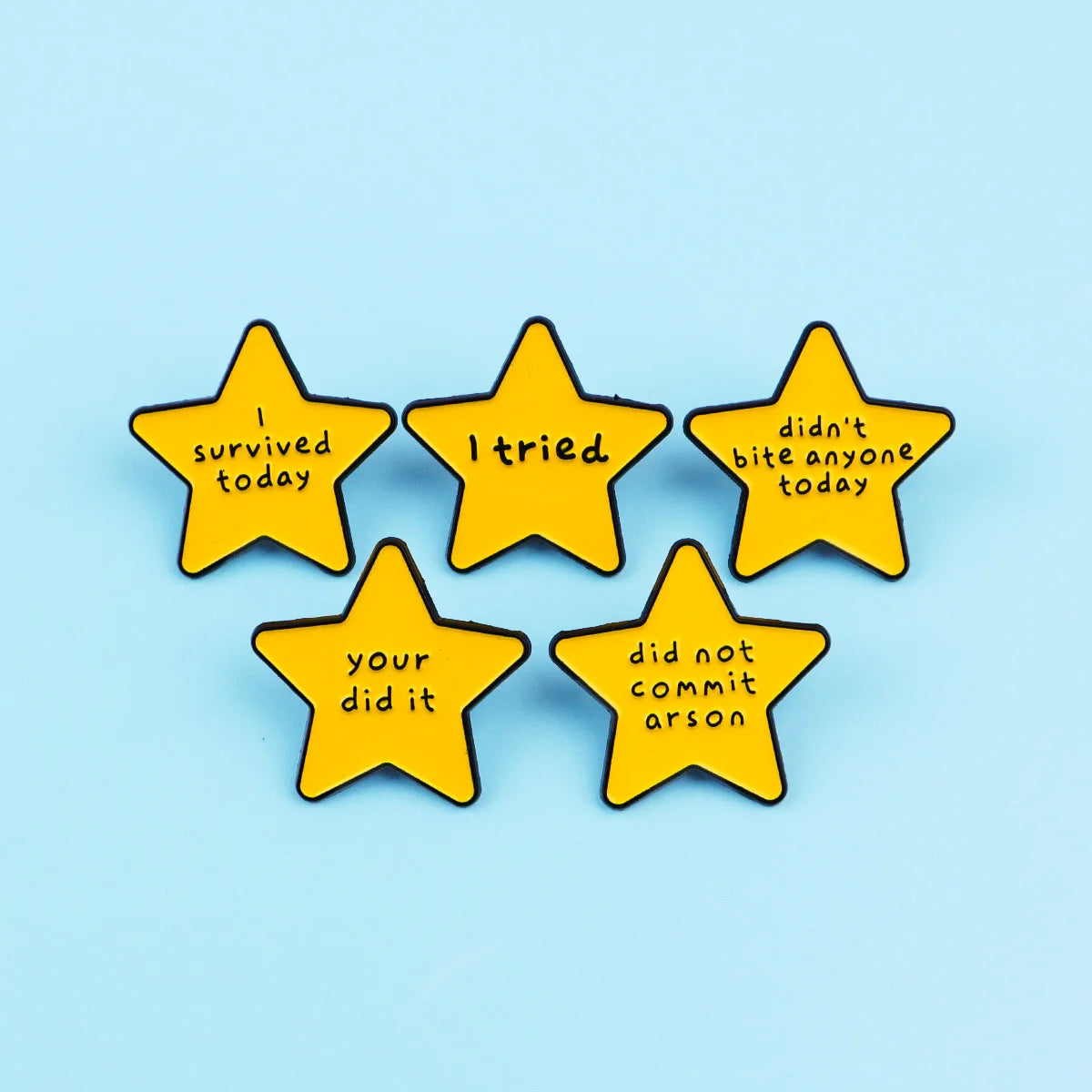 Five yellow star enamel pins with sarcastic quotes about surviving, trying, and not committing arson