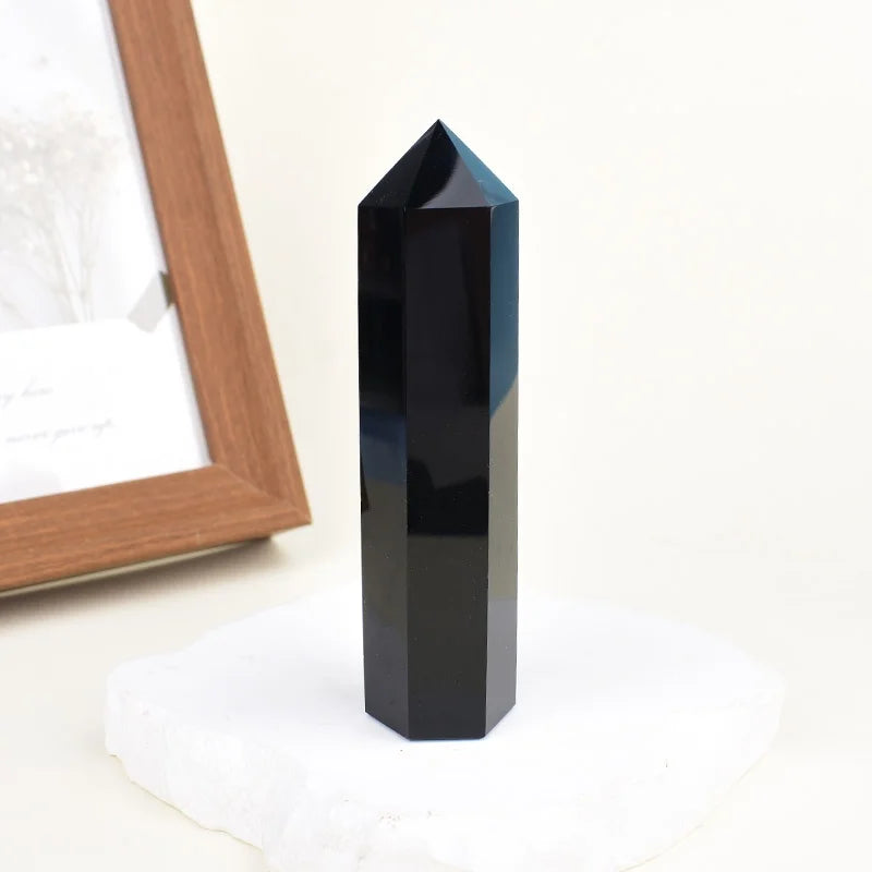 A black natural obsidian crystal obelisk point standing on a white surface.