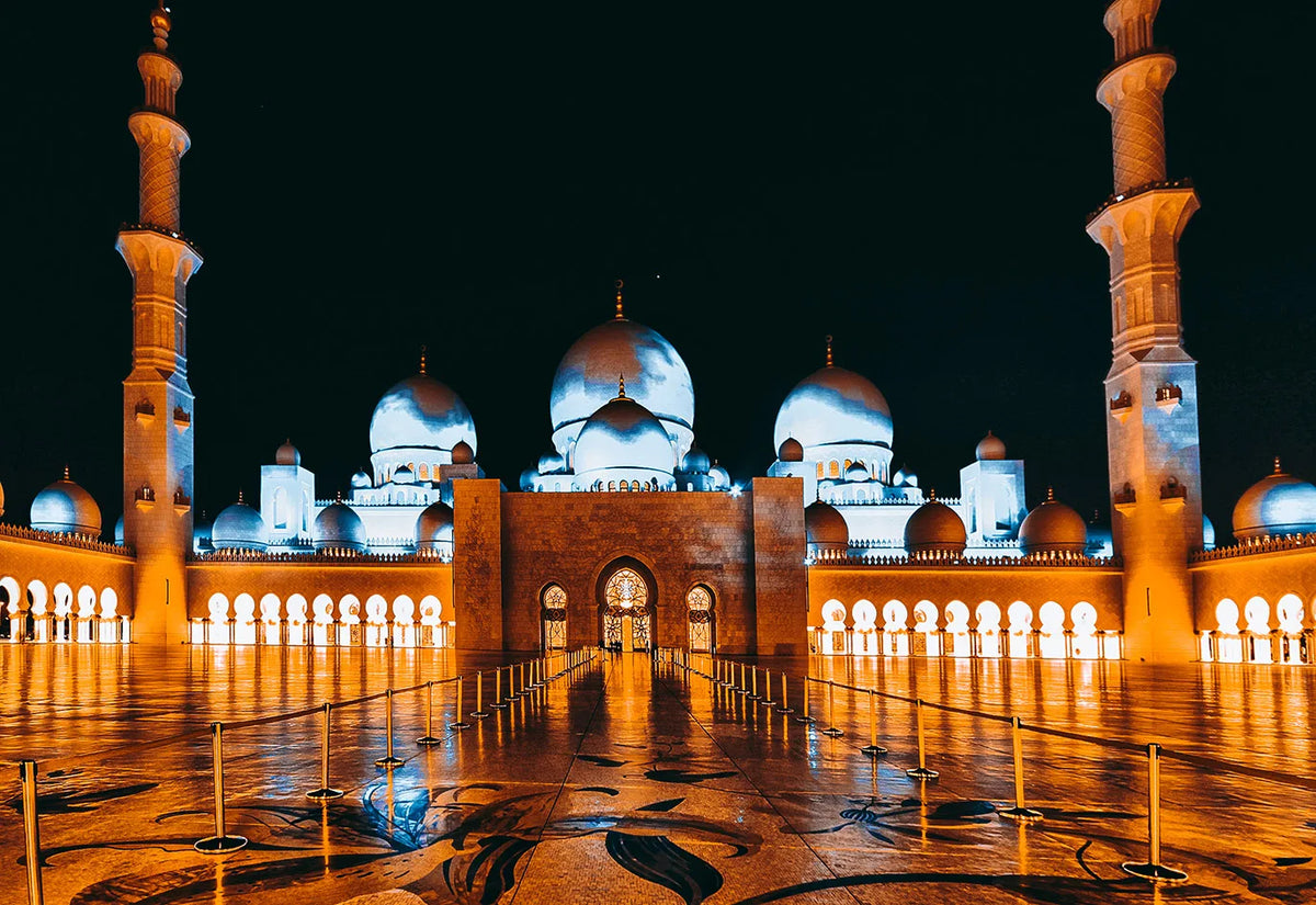 Night view of a mosque with golden domes and minarets reflected on the floor.