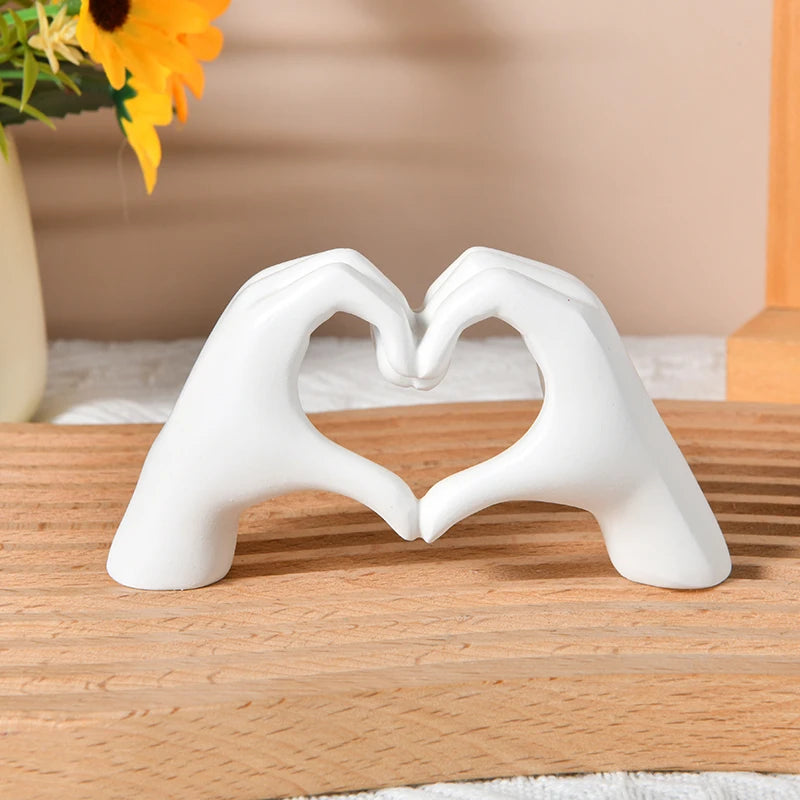 White sculpture of two hands forming a heart shape on a wooden surface