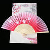 A pink and white vintage silk folding fan with delicate floral patterns displayed against a light background.