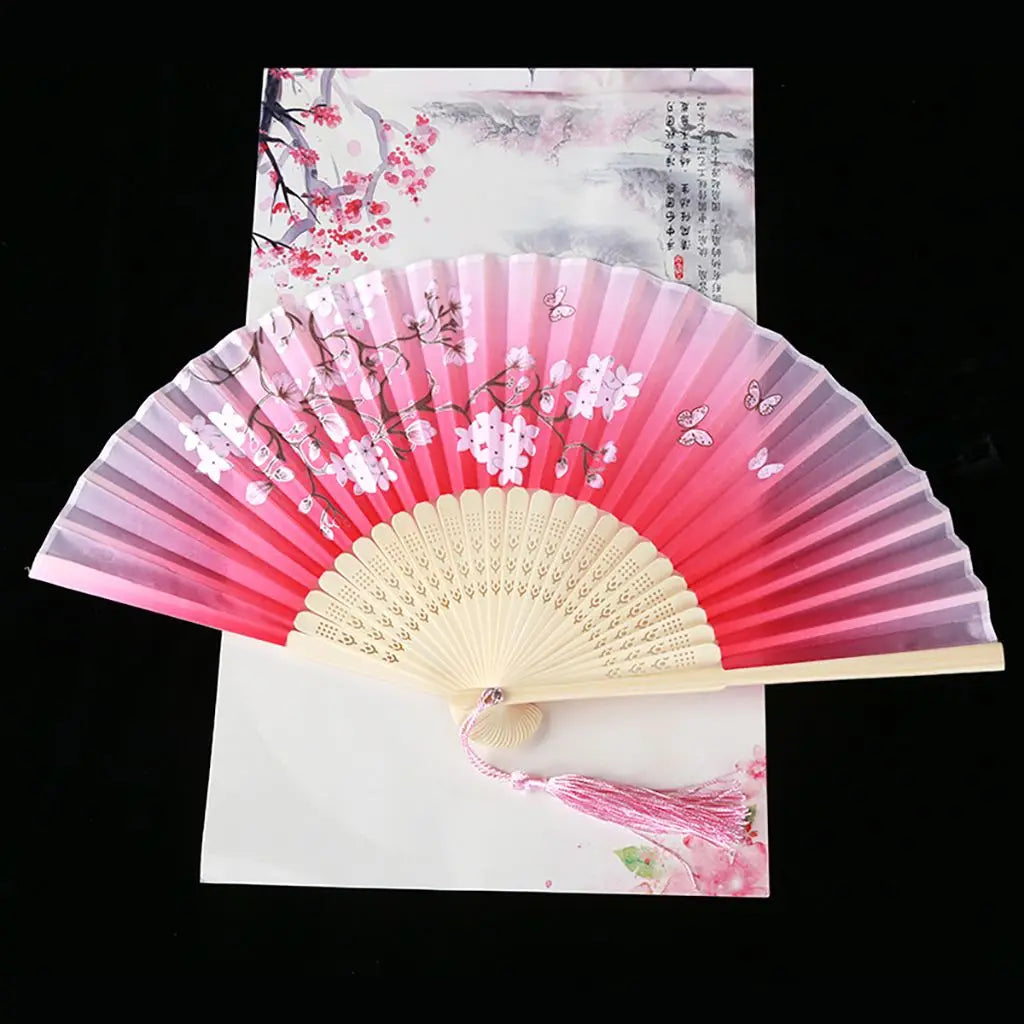 A pink and white vintage silk folding fan with delicate floral patterns displayed against a light background.