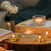 A collection of clear glass tealight candle holders and a white flower in a glass vase arranged on a wooden surface.