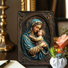 A metal sign depicting the Virgin Mary holding the infant Jesus, rendered in blue and gold tones.