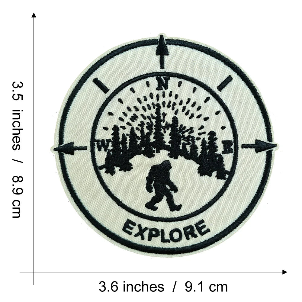 Black embroidered patch with the word EXPLORE inside a circular design featuring silhouettes of trees and a Bigfoot figure.