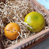 A bright yellow-green citrus fruit rests in a box filled with crinkle cut paper shred filler.