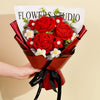 A bouquet of handcrafted red crochet roses in a red paper wrapping with a sign reading FLOWERS STUDIO