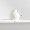 A white ceramic mini vase with a rounded body and narrow neck, shown on a shelf.