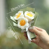 A hand holds a bouquet of handmade white crochet flowers with yellow centers, displayed against a blurred green background.