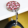 A round, red floral crystal handbag hook with a silver metal loop attached to a black leather strap.