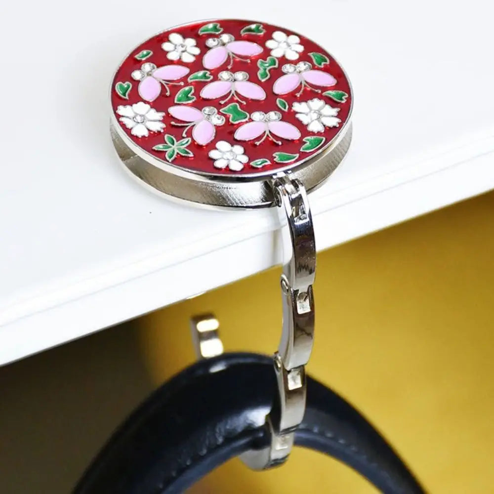 A round, red floral crystal handbag hook with a silver metal loop attached to a black leather strap.