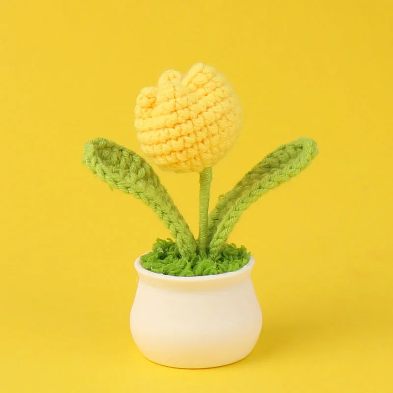 A hand-woven crochet flower in yellow sits in a white pot against a yellow background.